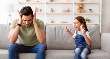 Ebeveynlik kavramı sorunları. Kızgın, yaramaz kızın portresi. Yorgun babasına bağırıyor ve bağırıyor. Kulakları tıkayan üzgün bir adam, histeriyi duymak istemiyor. Şok olmuş ebeveynle kavga
