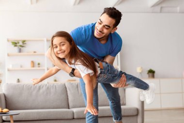 Mutlu anlar. Neşeli bir adamın elinde heyecanlı bir kızın portresi, kameraya bakıyor ve poz veriyor, eğleniyor, el çırpıyor, kanat çırpıyor, uçuyormuş gibi yapıyor, uçak taklidi yapıyor.