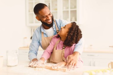 Pişirme Kavramı. Gülümseyen Afrikalı Amerikalı Baba ve Küçük Kızı 'nın birlikte mutfakta pasta hazırlarken, Adam, masanın üzerinde pul pul örerken, yemek pişirirken,