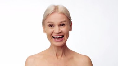 A mature woman in her 50s expresses joy, laughing. The bright background highlights her radiant smile and natural beauty, showcasing a moment of self-care and relaxation.