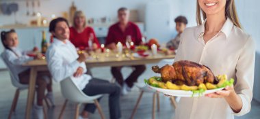 Şükran Günü ya da Noel için kızarmış hindi tutan mutlu genç bir kadın. Büyük bir aile için masa servisi yapıyor. Geleneksel bayramı evinde kutluyor.
