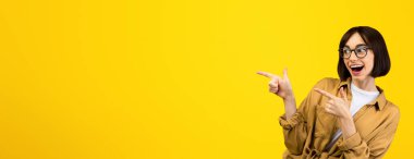 Turuncu stüdyo arka planı ve afiş için heyecanlı bir şekilde boş yeri işaret eden çok mutlu bir bayan. Neşeli kadın ürününüzün reklamını yapıyor, satışını veya indirimini destekliyor.