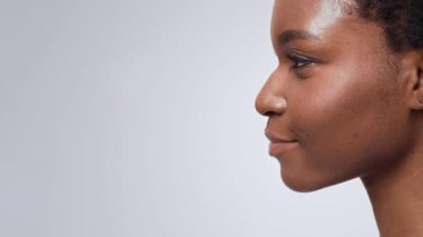 Afro-Amerikalı genç bir kadının profili temiz bir arka plana karşı durarak çarpıcı özelliklerini ve doğal güzelliğini vurguluyor. Onun profili zarafet ve özgüveni ifade ediyor, boşluğu kopyala