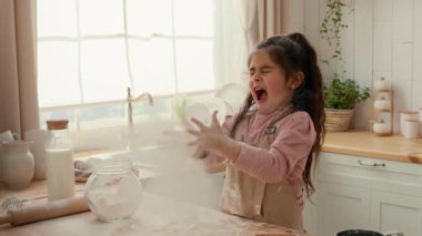 Genç bir kız neşe ve şaşkınlık ifade eder. Parlak bir mutfağa un atarken..
