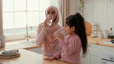 Sıcak bir mutfakta, bir anne ve küçük kızı bardaktan su yudumluyorlar. Sevecen hareketleriyle sevgi ve sıcaklık saçan bir neşe ve bağlantı anlarını paylaşıyorlar..