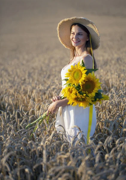 Meisje in tarwe veld met bloemen van zonnebloem — Stockfoto