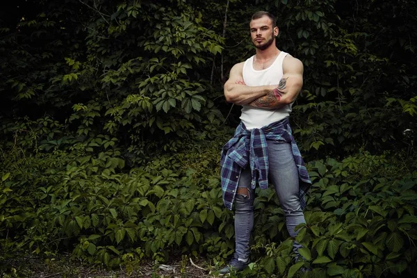 Handsome young masculine man posing outdoors in summer forest