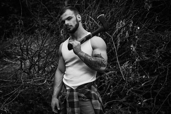 Black and white photo of handsome young man holding hatchet posing outdoors