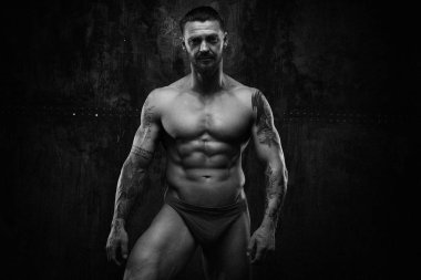 Siyah ve beyaz fotoğraf gömleksiz kaslı genç adamın grunge duvar arka planı poz 