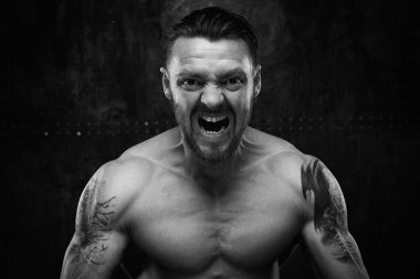 black and white photo of angry shirtless muscled young man screaming against grunge wall background  clipart