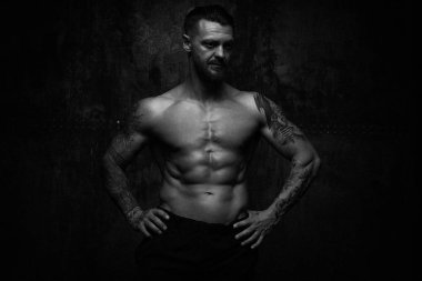 Siyah ve beyaz fotoğraf gömleksiz kaslı genç adamın grunge duvar arka planı poz 