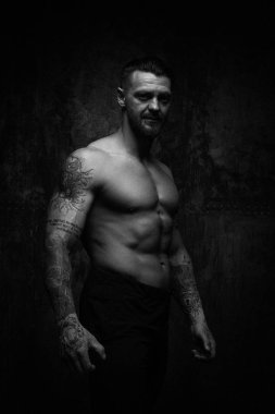 Siyah ve beyaz fotoğraf gömleksiz kaslı genç adamın grunge duvar arka planı poz 
