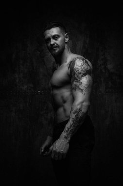 Siyah ve beyaz fotoğraf gömleksiz kaslı genç adamın grunge duvar arka planı poz 