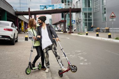 Kentsel arka plan üzerinde tekme scooter ile genç şık çift 