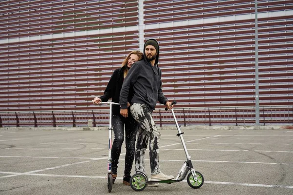 Kentsel arka plan üzerinde tekme scooter ile genç şık çift 
