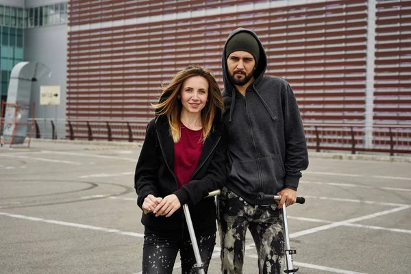 Young stylish couple with kick scooters on urban background