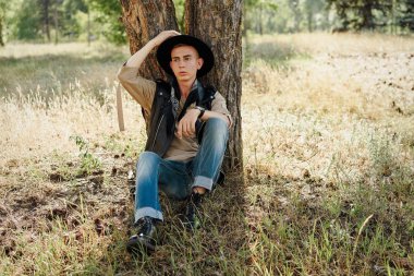 Yakışıklı genç adam rahat kıyafetler ve şık şapka açık havada poz 