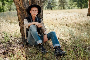 Yakışıklı genç adam rahat kıyafetler ve şık şapka açık havada poz 