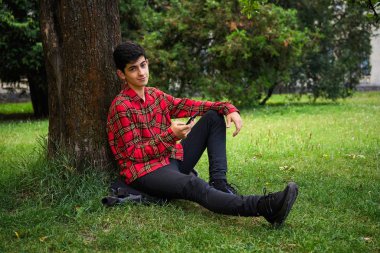 Telefon ile parkta çim üzerinde oturan genç adam.