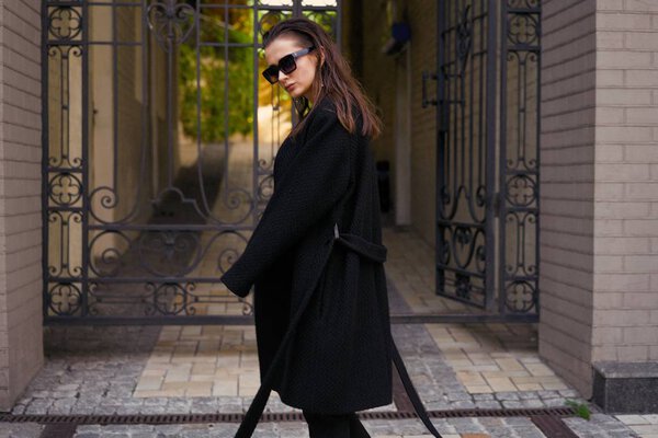 Прекрасная брюнетка в черной одежде позирует на улице.
 