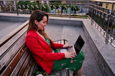 Park bankında otururken dizüstü bilgisayar kullanan genç güzel kadın