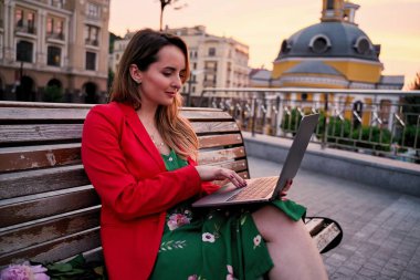 Park bankında otururken dizüstü bilgisayar kullanan genç güzel kadın