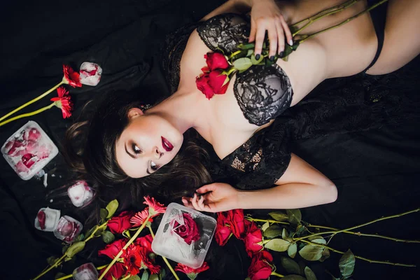 黒ランジェリー姿の若い女性が赤いバラを氷の中で凍らせて — ストック写真