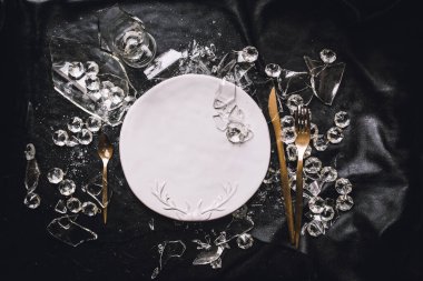 Tabak, altın kaplar, kristaller ve siyah arka planda kırık camlar.