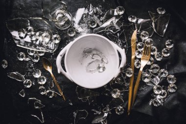 Beyaz tabak, altın kaplar, kristaller ve siyah arka planda kırık camlar.