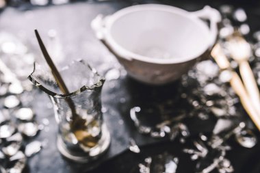 Kase, altın kaplar, kristaller ve siyah arka planda kırık camlar.