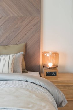 Klasik tarz yatak odası, iç tasarım konsepti, ahşap çalar saat ve modern lamba masa tarafında ahşap duvar dekorasyonu ile yatakta yastık kümesi