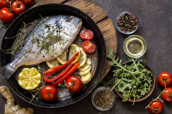 Dorado fish with fresh vegetables and herbs on a dark background