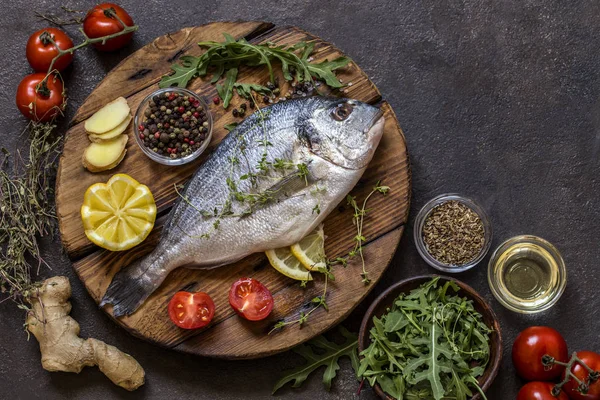 Dorado fish with fresh vegetables and herbs on a dark background