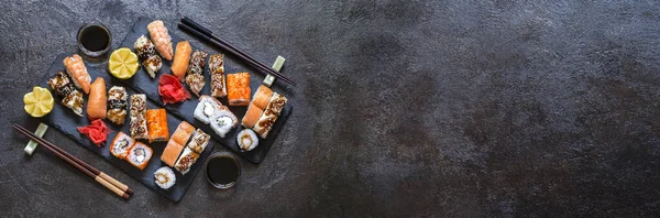 Suşi, pilav ve balıklı, soya sosu ve koyu taşlı arka plan.