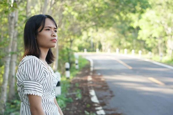 Asian woman waiting for a bus on the side of the road