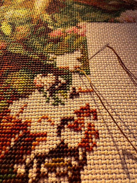 A close-up shot of an in-progress embroidery piece, highlighting the needle and thread, and the rich, colourful texture of the crafted fabric.