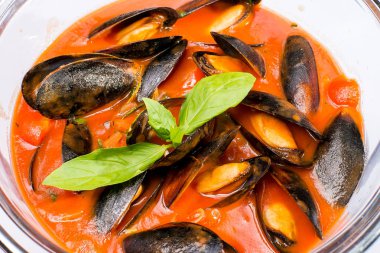 Yuvarlak bir tabakta Fesleğen ile süslenmiş domates soslu midyeler