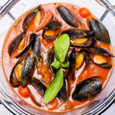 Yuvarlak bir tabakta Fesleğen ile süslenmiş domates soslu midyeler