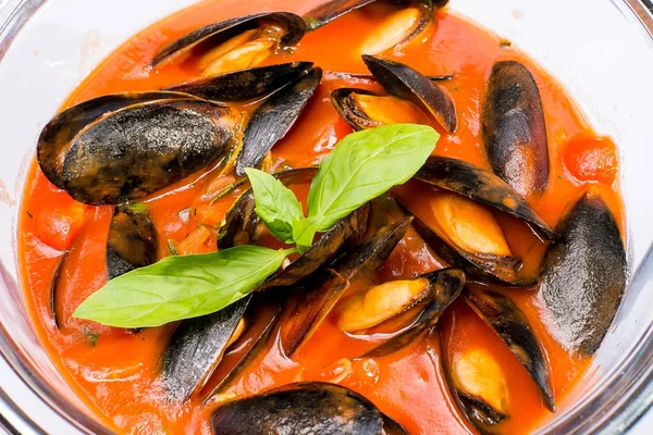 Yuvarlak bir tabakta Fesleğen ile süslenmiş domates soslu midyeler