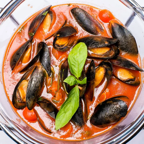 Yuvarlak bir tabakta Fesleğen ile süslenmiş domates soslu midyeler