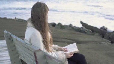 Genç bir kız akşam gün batımında bir kitap tarafından deniz okuma bir bankta oturur. gün batımında sahilde okuma 4 k. A çocuk. Deniz kenarında bir kız rahatlatıcı sahil şeridi.