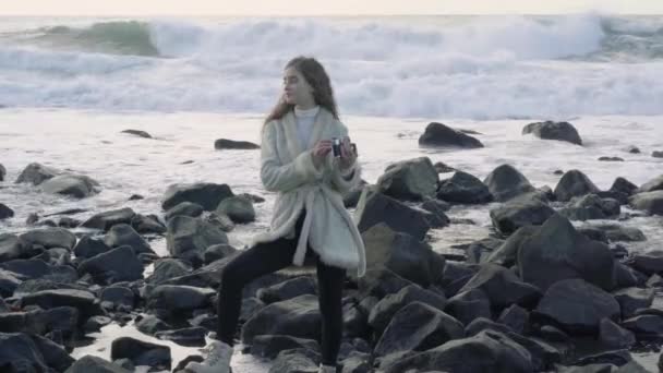 Fille photographe sur le rivage de la mer orageuse fait des photos. Voyageur touristique photographe faisant des photos océan. Mer orageuse avec nuages orageux. Instantanés d'un voyage à la mer.4k.30fps . — Video