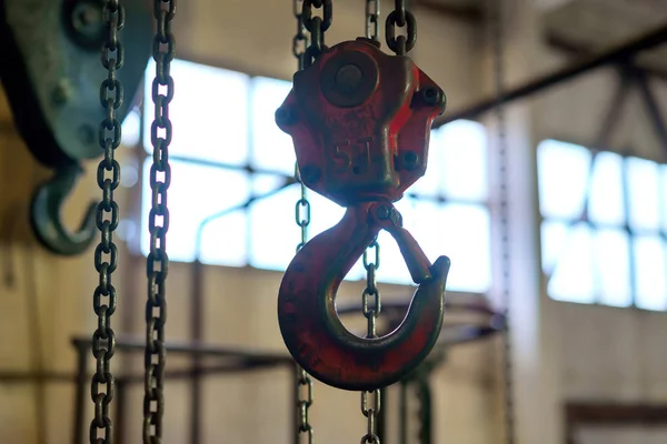 a red crane hangs from the ceiling on a chain in the room for lifting and moving heavy loads to the sides.