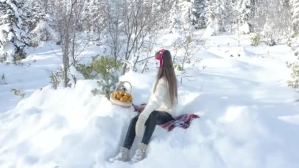 一个年轻女孩带着一篮戴着耳机的普通话走在冬林里 圣诞老人 — 图库视频影像