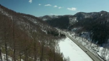 Kışın ormanın havadan görünümü parlak güneşli bir günde bol kar, tepelerde yola yolun kuş bakışı görünümü.