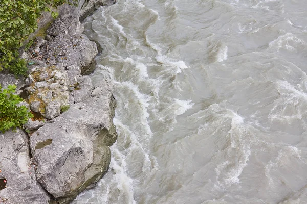 a shallow fast river with dark water, part of the water covers the stones, and part of the green algae that are under water, the top view, out of focus