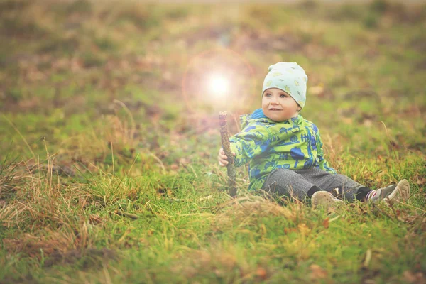 Menino pequeno está sentado na grama e segurando varinha mágica com luz — Fotografia de Stock