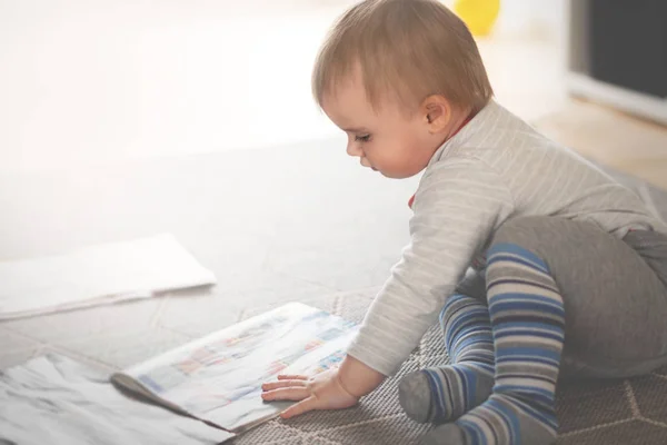 Niño pequeño está sentado en el suelo y leyendo revistas, foc poco profundo —  Fotos de Stock