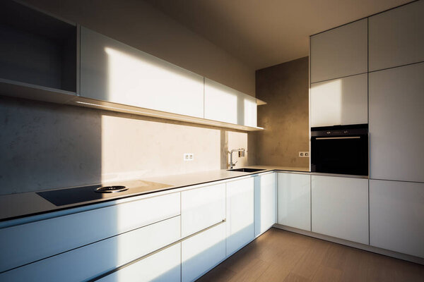 New modern white kitchen in minimalist design, during morning sunrise hour, with modern appliances, wall-sockets and premium materials such as glass, concrete, stainless steel and wooden floor. 