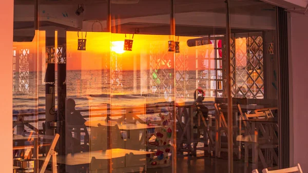 Seaside landscape - view of the coastal cafe with the reflection in glass of sunrise over the sea, city of Varna, on the Black Sea coast of Bulgaria